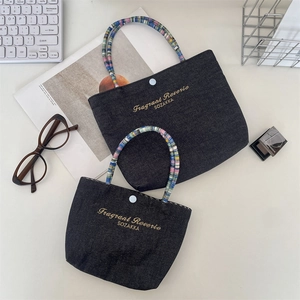 Close-up of denim handbag featuring colorful beaded handles and gold embroidery detail