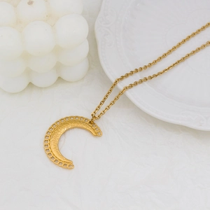 Gros plan d'un collier croissant de lune doré aux motifs ajourés sur papier texturé blanc