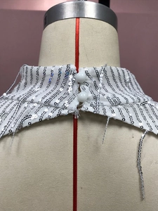 Detalle de vestido blanco con lentejuelas plateadas, cuello alto y cierre de botones atrás