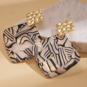 Close-up of geometric acrylic earrings with marble texture on white plaster base