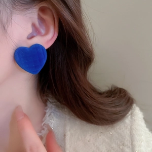 Close-up of blue flocked heart earrings worn by a model with soft lighting and hair