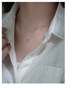 Close-up of a minimalist silver bean pendant on a delicate chain worn by a model