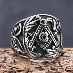Gros plan d'une bague maçonnique argentée avec le symbole G et l'équerre sur bois