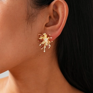 Close-up of golden firework stud earring with red enamel and white zircon on a model