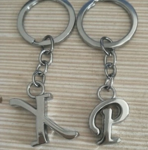 Close-up of silver metal alphabet keychains with letters K and P on a wooden surface