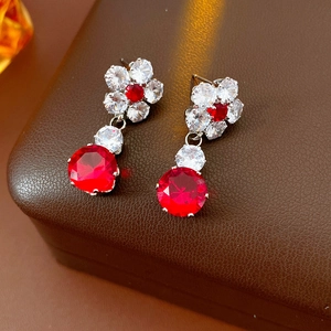 Detail of flower earrings with red and white zircons on a textured jewelry box