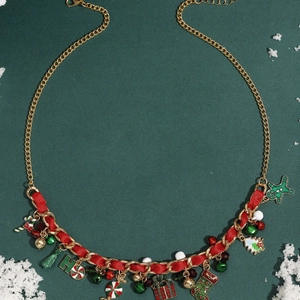 Golden Christmas charm necklace with red ribbon, bells, and holiday trees on green background