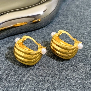 Macro shot of gold metal earrings with embossed texture and elegant white pearls