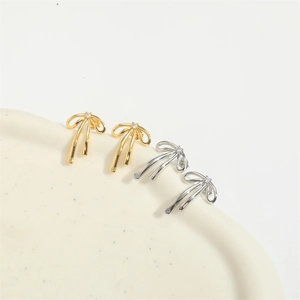 Macro detail of gold and silver bow earrings with zircon stones on a beige tray