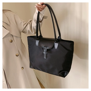 Detail of black nylon tote bag featuring premium leather trim and metal buckle closure