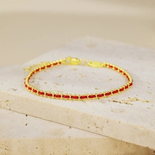 Detail of red rope and gold bead woven bracelet with lobster clasp on beige stone