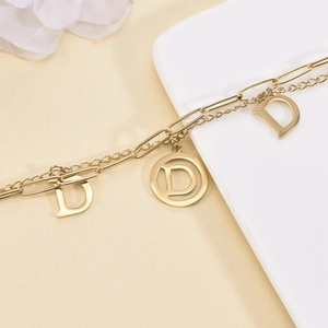 Double-layered gold titanium steel bracelet with hollow D-letter charms on beige decor
