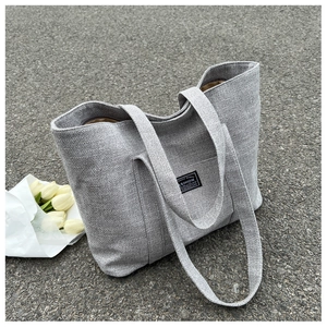 Detail shot of grey textured tote bag with fabric logo patch and white tulips on pavement