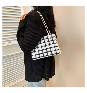 Close-up of black and white plaid tweed crossbody bag with gold chain strap on model
