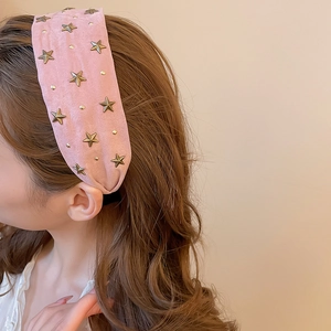 Gros plan d'un serre-tête rose en tissu avec étoiles dorées sur des cheveux bruns doux