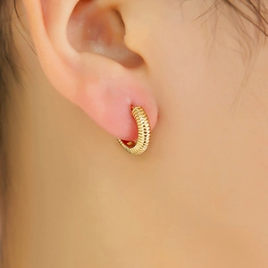 Détail de boucles d'oreilles créoles dorées avec texture rainurée portées sur l'oreille