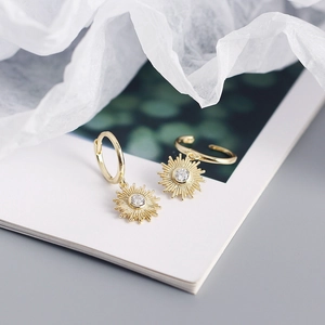 Detailed view of gold sunburst earrings with sparkling zircon centers on a white surface