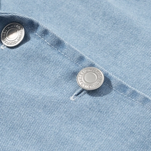 Detailaufnahme von blauem Jeansstoff mit hochwertigen gravierten silbernen Metallknöpfen