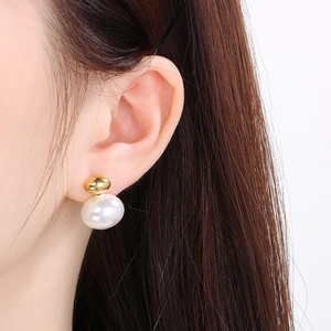Detailed close-up of a white oval shell earring with gold bead stud on model's ear