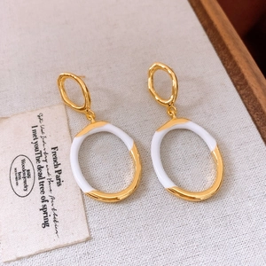 Detail of drop earrings with interlocking gold and white enamel oval rings on beige fabric
