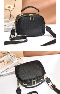 Detail view of black crocodile pattern PU leather bag with wide striped strap and gold hardware