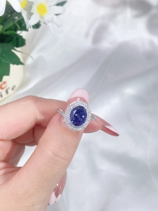 Close-up of a silver ring featuring a large oval blue gemstone with double halo of diamonds