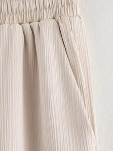 Détail de la taille élastique et poche latérale sur pantalon plissé en lin beige