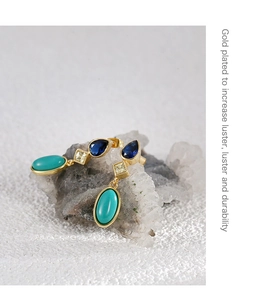 Macro detail of gold-plated drop earrings with blue and green zircon gemstones