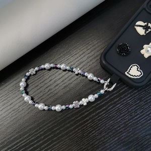 Detail of beaded phone strap with white pearls and silver rose charms on black background