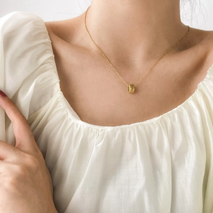 Close-up of a minimalist gold cylindrical pendant necklace on a woman's collarbone