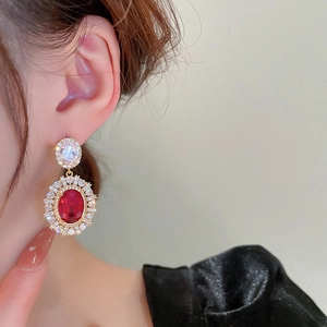 Macro shot of luxury red gemstone earrings with floral diamond accents on model