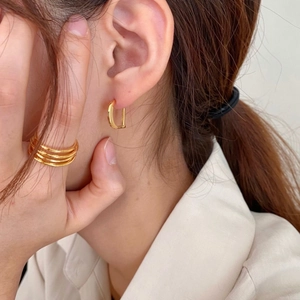 Detail of a gold D-shaped hoop earring and layered ring set on model skin