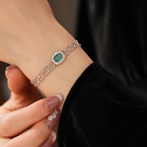 Detailed close-up of a silver-toned bracelet with a green oval gemstone and halo diamonds