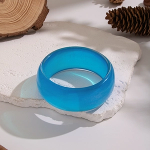 Close-up of translucent blue geometric wide bangle on white stone and pinecone