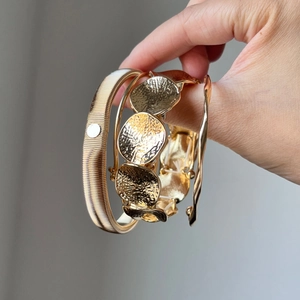 Three-piece gold geometric bangle set including woven and hammered textures held by hand