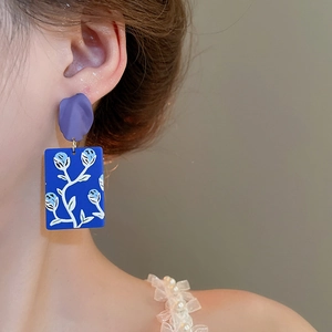 Detail view of retro floral matte rectangle drop earrings worn on a model's ear