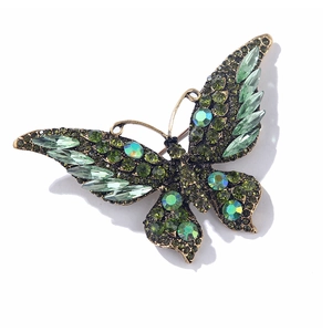 Detailed close-up of vintage crystal butterfly brooch with green rhinestones and gold base