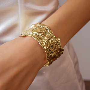 Detailed close-up of a wide hammered gold cuff bracelet with textured lava finish