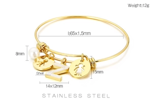 Detail view of gold adjustable steel bracelet with Z pendant, pearl and hollow figures