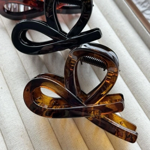 Glossy bow hair claw clips in black and tortoiseshell finish on beige fabric