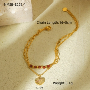 Detail of gold double-layer chain bracelet with red beads and heart pendant on stone surface