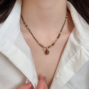 Close-up of Maillard style gold plated tiger eye necklace on a female neck with white shirt