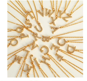 Detailed flat lay of golden titanium necklaces with crystal paved alphabet pendants