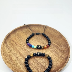 Détail de bracelets en perles d'obsidienne avec lettres A et M sur plateau bois