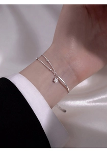 Detail of silver star charm bracelet on a model wrist with elegant silk background