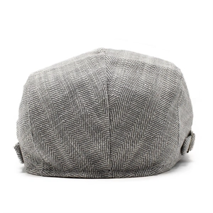 Detail of gray herringbone newsboy cap featuring adjustable bronze metal side buckles
