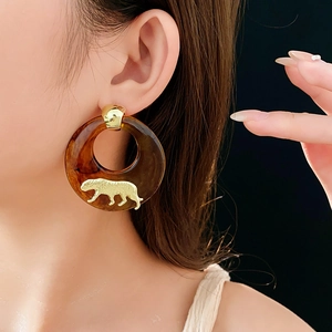 Detailed view of amber resin hoop earring with gold leopard emblem worn by a model