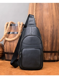 Detail of black textured leather sling bag with front zipper on a vintage wooden background