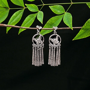 Detailed view of silver butterfly tassel earrings hanging on natural green branches