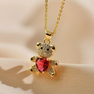 Golden teddy bear pendant necklace with red heart gemstone on champagne silk background